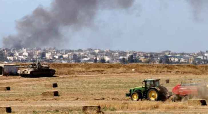 Agricultural vehicle harvests hay in front of army tank on Gaza border